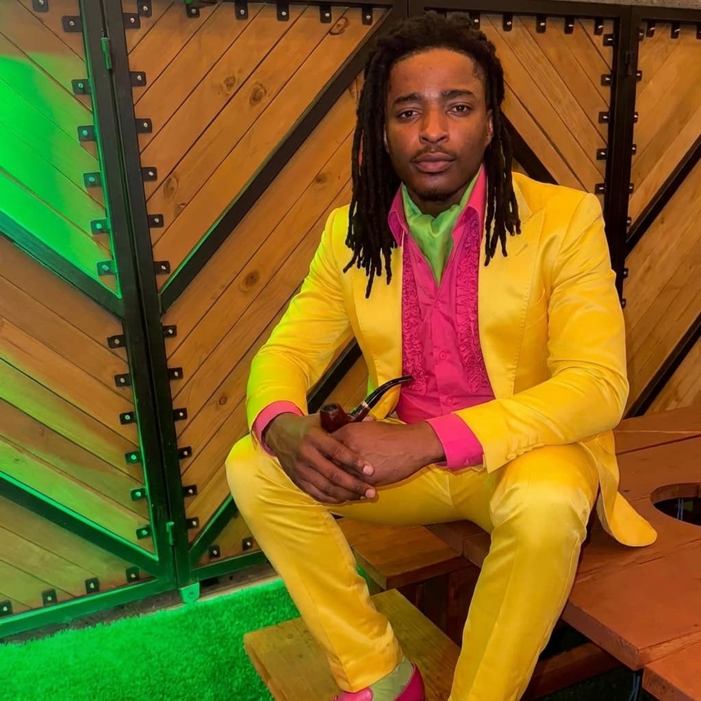 put man sitting down in yellow outfit matching lighting and stance of man in yellow outfit and location no glasses keep facial structure of man sitting down