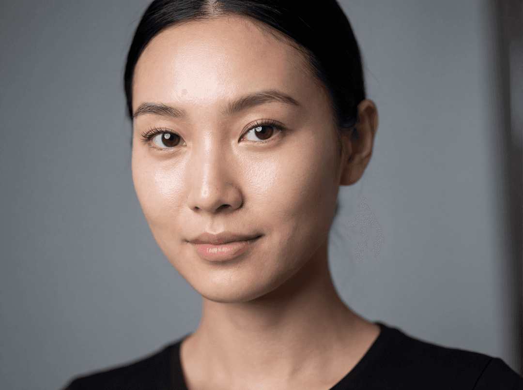 **Subject:** An East Asian fashion model, approximately 20-25 years old, with a sophisticated and serene expression. Her facial features are meticulously rendered:
    *   **Skin:** Flawless, luminous, and subtly dewy, showcasing individual pores and a natural skin texture. No heavy makeup, allowing her natural complexion to shine through.
    *   **Eyes:** Large, almond-shaped, with a deep, contemplative gaze. Visible catchlights in her pupils, reflecting the light source. Long, delicate eyelashes are clearly defined, and subtle, natural-looking lower lashes are present. Her eyebrows are perfectly groomed, with individual hairs visible.
    *   **Nose:** A delicate, well-defined bridge and nostrils.
    *   **Lips:** Full, naturally rosy, with a soft, matte texture. Subtle creases and a slight wetness are visible.
    *   **Hair:** Sleek, dark, and styled in a minimalist, elegant manner, perhaps pulled back or parted cleanly, framing her face without obscuring features. Individual strands are discernible.

**Lighting:** Soft, diffused, and even studio lighting that highlights the contours of her face and creates subtle shadows, emphasizing depth and realism. A very subtle rim light might be present to separate her from the background.

**Composition:** A tight, ultra-realistic headshot, filling the frame. The focus is entirely on her face, with no distracting elements.

**Photography Style:**
    *   **Camera:** High-resolution professional DSLR or mirrorless camera (e.g., Sony Alpha 1, Canon R5, Nikon Z9).
    *   **Lens:** A prime portrait lens (e.g., 85mm f/1.4, 100mm f/2.8 macro) to achieve extreme sharpness and subject isolation.
    *   **Aperture:** Wide open (f/1.4 - f/2.8) for a shallow depth of field, ensuring only her face is in sharp focus, with a creamy, soft bokeh in the background.
    *   **Shutter Speed:** Fast enough to capture every detail without blur.
    *   **ISO:** Low, to minimize noise and maximize image quality.

**Post-Processing:** Minimal and natural. No heavy retouching or airbrushing. The goal is to enhance the existing realism, not to create an artificial perfection. Subtle color grading to achieve a natural, pleasing aesthetic.

**Aesthetic:** High-end editorial, luxury fashion, showcasing natural beauty and exquisite detail.

**Keywords:** Ultra-realistic, hyperrealistic, photorealistic, detailed, intricate, sharp focus, natural light, studio portrait, fashion photography, beauty shot, high-resolution, professional, editorial, exquisite detail, pores, skin texture, individual hairs, catchlight, natural beauty, authentic, unretouched, vogue, harper's bazaar.