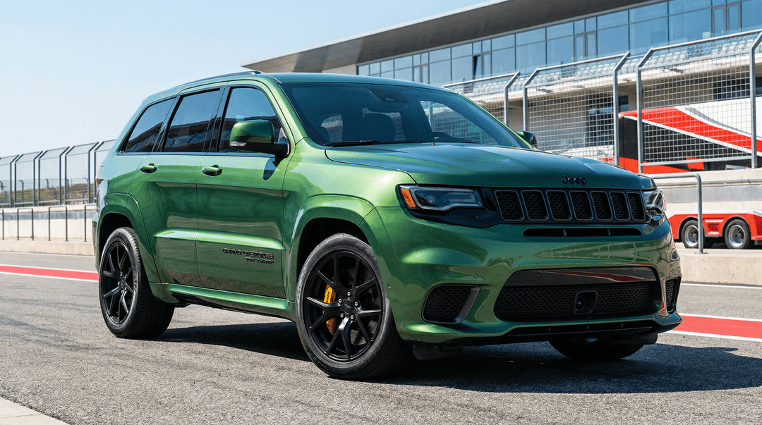 A vibrant, metallic emerald green Jeep Grand Cherokee Trackhawk parked at a professional racetrack under bright daylight, captured from a dynamic three-quarter front angle that emphasizes its aggressive stance and glossy, mirror-like paint finish reflecting the sky and surrounding structures. The SUV features blacked-out trim, a bold seven-slot grille with “Jeep” lettering, sleek LED headlights, and a performance-oriented front splitter. The side displays “Grand Cherokee Trackhawk” badging in black lettering, with large multi-spoke black alloy wheels wrapped in low-profile tires and bright yellow Brembo brake calipers visible behind them. The vehicle sits on smooth asphalt with red and white curbing along the edge of the track, and in the background, a modern pit lane building with glass windows and garage doors is visible, along with a safety fence and a partially visible red-and-white race car transport trailer. The lighting is crisp and high-contrast, highlighting the car’s curves and reflections with cinematic realism. The scene conveys speed, luxury, and high-performance engineering, rendered in ultra-high detail with photorealistic textures and vibrant color saturation. Style: automotive editorial photography, professional car shoot, dynamic composition, shallow depth of field, studio-quality lighting.
