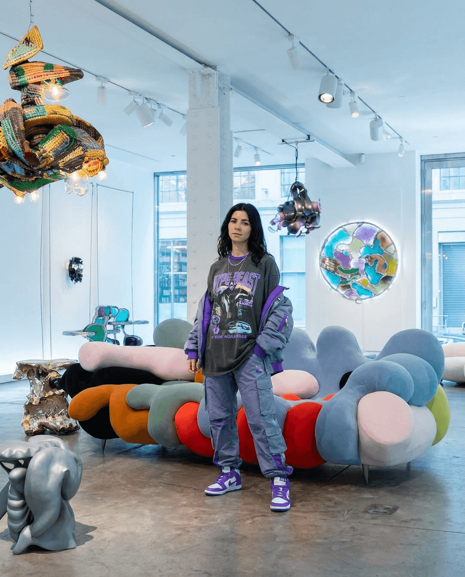 Lifestyle context shot setting the scene for Siam in HYPE BEAST COMBO: MARINA is present naturally in the environment, soft natural light, hints of the accent color #7c3aed, medium-pace cinematic mood,  editorial photography, no visible logos — preserve EXACT location identity: contemporary art gallery with white walls and exposed ceiling beams (indeterminate) — mixed soft and specular cool daylight light — white structural columns, polished concrete floors.