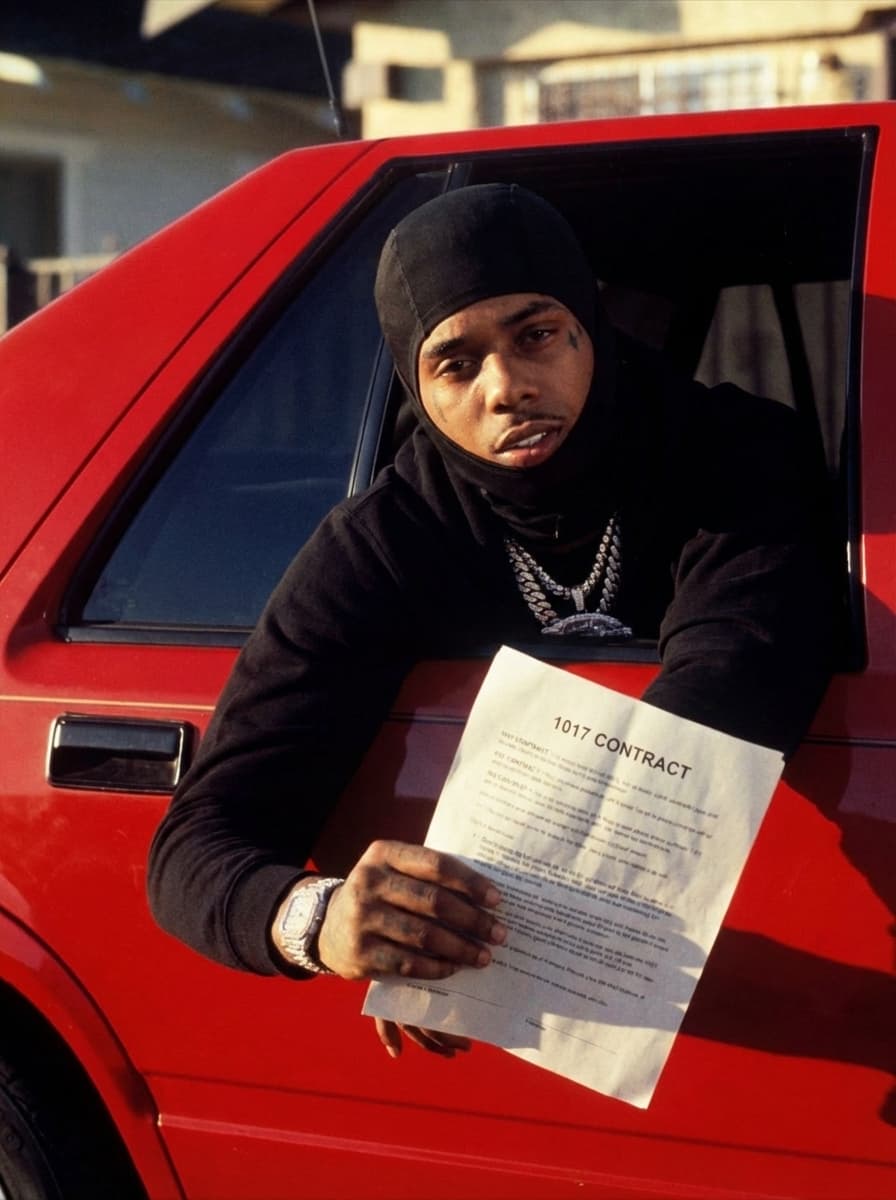 Use Image 1 (car scene) as the base environment and composition. Use Image 2 (masked rapper) as the character reference.  CORE INSTRUCTIONS: Replace the original subject in Image 1 with the person from Image 2 Maintain the exact same pose, angle, framing, and body positioning from Image 1 (leaning out the car window) Keep the red car, background, lighting, and cinematic tone identical CHARACTER DETAILS: Apply the exact facial features, skin tone, tattoos, and identity from Image 2 Keep the black ski mask (Shiesty mask) exactly as shown in Image 2 Preserve jewelry (chains, watch) for realism Maintain a serious, focused expression ACTION CHANGE: REMOVE the shotgun completely Replace it with a document held in both hands, matching the same angle and grip position DOCUMENT SPEC: Paper should clearly read: “1017 CONTRACT” Realistic paper texture (slight folds, natural lighting, shadows) Positioned exactly where the weapon was for natural realism STYLE & QUALITY: Ultra-realistic cinematic photography 35mm film still look Warm tones, high contrast Slight film grain Natural shadows + highlights matching original lighting No AI distortion, no cartoon look