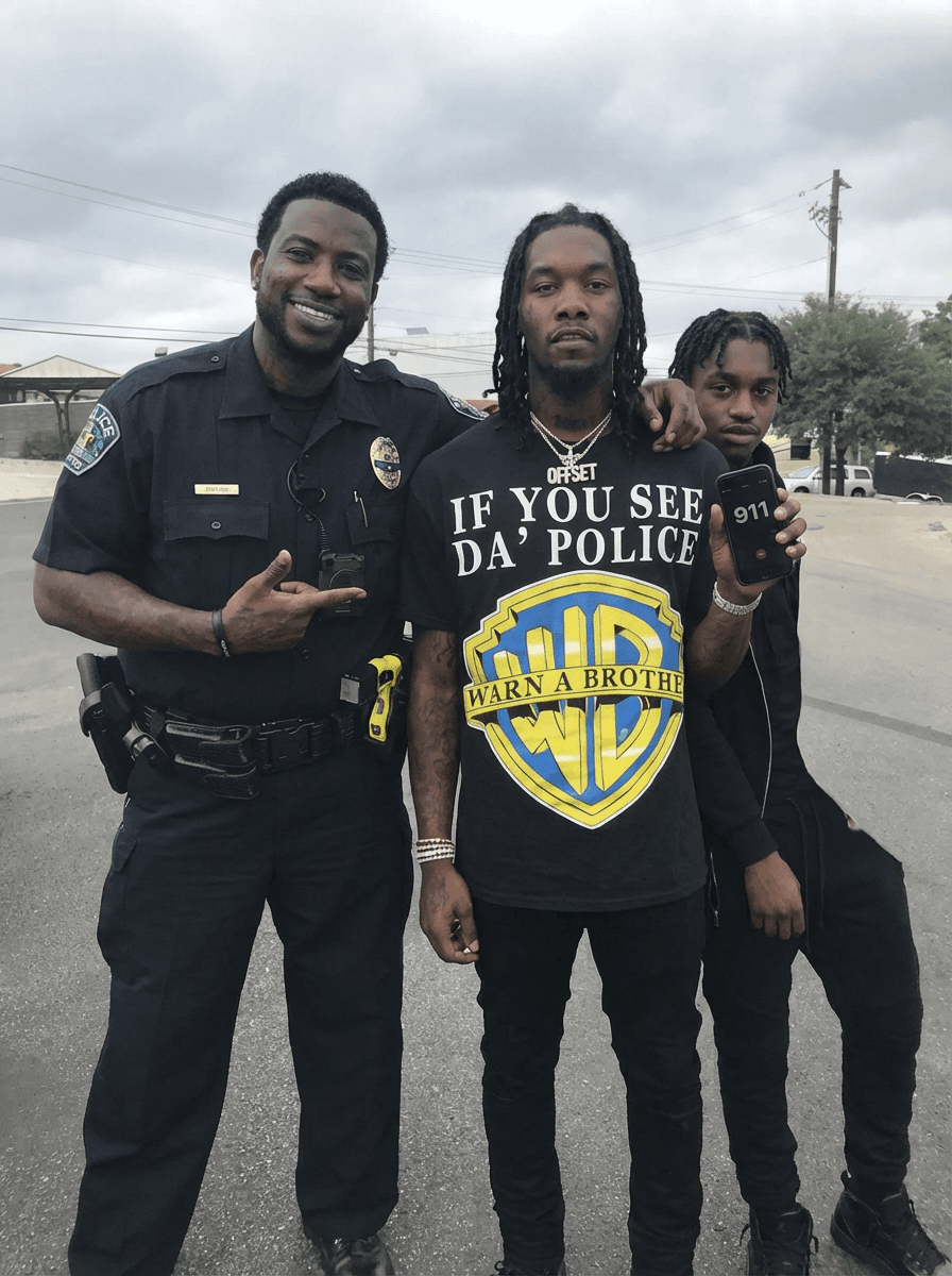 Use the provided image as the base reference. Maintain the exact same environment lighting, camera angle, pose, outfit structure, and composition from the original image. Replace the original subject with OFFSET THE RAPPER AN GUCCI MAN WITH A BLACK FAT COP  wearing outfits attached HOLDING A PHONE WITH 911 ON IT WITH LIL TJ NEXT TO HIM
