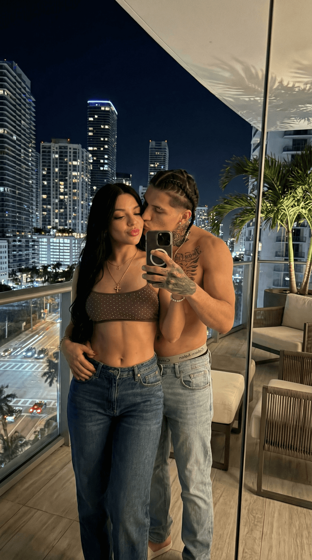 i would like to have this exact same guy and the girl in the exact same pose but instead of taking a mirror pic in the bathroom make a mirror pic in the top of a miami balcony penthouse with city view at night
