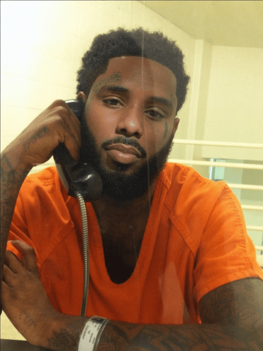 replace the man on phone in jail face with pooh shiesty (refence man) keeping lighting changing nothing else keep reference man facial hair in swap keep lighting and bad quality of jail photo and keep face proportionate