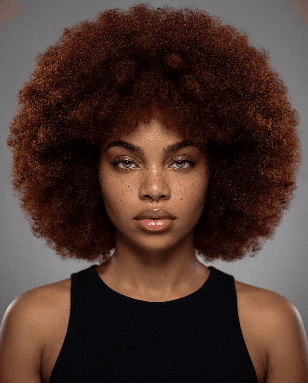 A hyperrealistic photograph, studio lighting, detailed, headshot of a stunning Black woman, her face a canvas of strength and beauty. Her natural Afro, voluminous and perfectly shaped, frames her face, with a rich, deep auburn hue. The catchlights in her eyes reflect a subtle intensity, and her skin, flawlessly smooth, glows under the expert lighting. The background is a soft, diffused studio grey, allowing her to be the sole focus. The image is sharp, with incredible detail in her hair texture and skin, as if captured by a high-end Hasselblad with a 85mm f/1.2 lens.