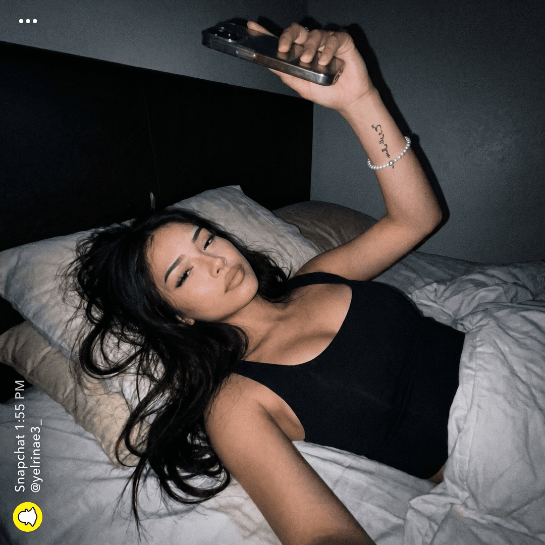 Make a unique combination of these females on a bed selfie like Snapchat baddies upward postion while she laid back in bed with a darker background quality can be little shaky but clear like a realistic bed selfie would b but nonchalant expression not too much make up we want a realism look can the angle be more from the top position up kinda like she's laying on  a bed make eyes little more squinted 