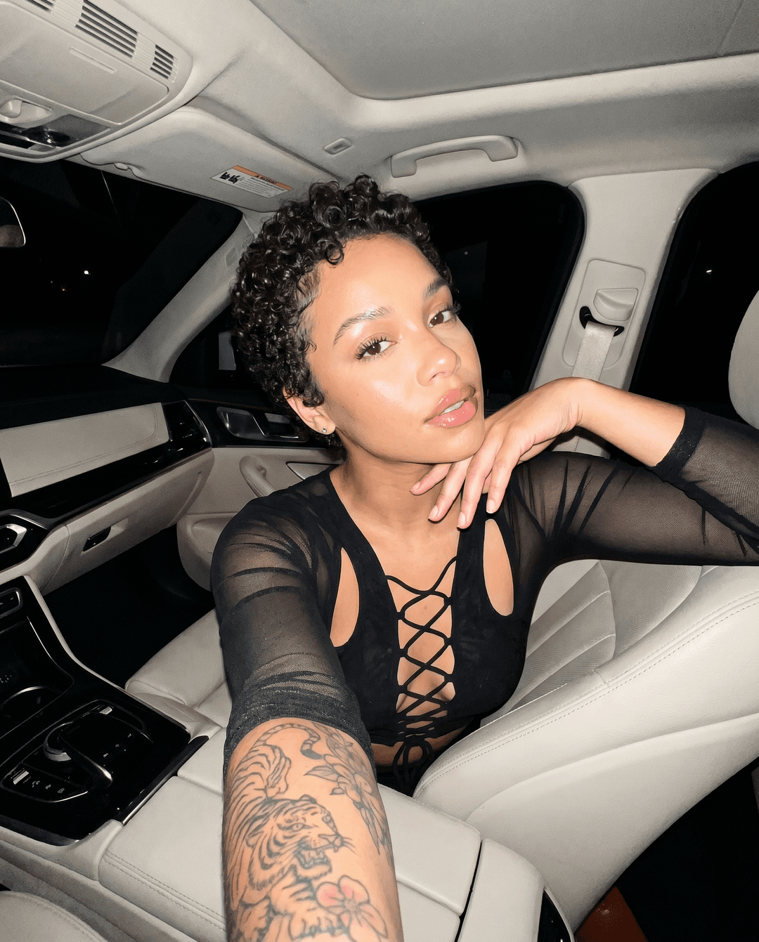 {
  "tool": "nano_banana_pro",
  "aspect_ratio": "4:5",
  "mode": "text-to-image",

  "identity_lock": "Naomi Solei EXACT identity only — preserve exact facial structure, skin tone, proportions, and signature features from Omni reference",

  "identity_protection": "NO substitution, NO lighter skin drift, NO ethnicity change, NO alternate face generation",

  "body": "curvy feminine build, small defined waist, full round glutes, full bust, realistic proportions",

  "hair": "short natural curly pixie cut ONLY, tight curls with soft shine and clean edges",

  "hair_rule": "DO NOT generate long straight hair, wigs, lace fronts, or loose waves under any condition",

  "tattoo": "Naomi Solei signature tattoo on RIGHT arm only — partially visible naturally depending on crop and sleeves",

  "scene": "luxury car interior at night, parked, dim environment outside windows, premium cream leather seats",

  "composition": "close-up chest-up selfie framing, slight high-angle phone selfie perspective, intimate luxury nightlife vibe",

  "pose": "Naomi seated in passenger seat, one hand resting near chin, relaxed confident posture",

  "expression": "soft seductive confidence, glossy lips, calm direct eye contact",

  "outfit": {
    "top": "black lace-up fitted nightlife top with mesh sleeves and cutout details",
    "fabric": "stretch satin and mesh textures with realistic tension and folds"
  },

  "lighting": {
    "source": "direct iPhone flash inside dark car",
    "behavior": "sharp flash highlights on skin and hair with deep surrounding shadows",
    "rule": "must feel like real nighttime flash selfie, not studio glam lighting"
  },

  "camera": {
    "type": "iPhone 15 Pro Max",
    "lens": "front camera",
    "style": "raw flash selfie",
    "perspective": "natural handheld arm-length framing"
  },

  "details": [
    "visible skin texture",
    "natural flash reflections in eyes",
    "subtle grain from low-light capture",
    "realistic leather seat texture",
    "slight exposure clipping from flash",
    "defined lashes and glossy lips"
  ],

  "environment_details": [
    "luxury car stitching visible",
    "night darkness outside windows",
    "realistic dashboard shadows",
    "authentic low-light atmosphere"
  ],

  "override_rules": [
    "NO identity drift",
    "NO long hair",
    "NO ethnicity changes",
    "NO unrealistic anatomy",
    "NO beauty filter",
    "NO CGI-looking lighting"
  ],

  "realism": "ultra photorealistic raw iPhone flash selfie, authentic nightlife energy, must feel genuinely captured and not AI generated"
}