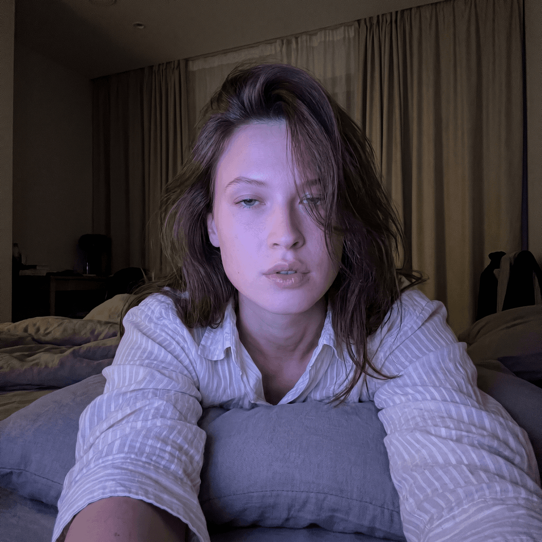 <faceid:3983732:1.0> { "meta": { "aspect_ratio": "9:16", "quality": "ultra_photorealistic", "resolution": "8k", "camera": "iPhone 15 Pro Max front camera", "lens": "24mm wide", "style": "raw iPhone selfie realism, not studio, not professional, visible natural texture" }, "character_lock": { "face_identity": [ "same as reference image", "same facial proportions, same jawline", "NO face change, NO face swap errors" ], "skin": [ "pale porcelain skin tone", "smooth but real texture", "not plastic, not over-smoothed", "soft glow on cheeks" ], "hair": [ " hair", "messy bedroom hair", "side-part with strands falling over one eye", "slightly shiny strands, soft volume" ] }, "scene": { "location": "dim bedroom at night", "environment": [ "dark background", "soft shadows", "beige blackout curtains on left side", "bed vibe, cozy messy room feeling" ], "atmosphere": "late-night sleepy lo-fi, intimate quiet mood" }, "lighting": { "type": "low-light cool glow", "key_light": "cool bluish-purple glow on face", "fill_light": "very soft ambient darkness", "contrast": "high contrast, face lit but background nearly black", ] }, "camera_perspective": { "pov": "arms length selfie", "angle": "slightly low angle close-up selfie", "distance": "very close, intimate framing", "framing": "face + upper chest, cropped tight, arm extended and leaving the frame at the edge", }, "subject": { "gender": "female", "age": "21+ (adult)", "vibe": "effortlessly hot, sleepy, soft but dangerous", "expression": { "eyes": "heavy-lidded dreamy stare", "mouth": "slightly open, relaxed lips", "emotion": "tired + seductive without trying" }, "pose": { "position": "lying on stomach", "support": "propped up on grey pillow with subtle pattern", "hand": "hand near face, index finger touching lower lip" }, "outfit": { "top": { "type": "extremely cropped white tank top / tee", "fit": "skin-tight, stretched thin, riding up high", "details": "thin fabric, realistic tension folds, visible through material", "underwear": "no bra" }, "extra": [ "denim jacket completely slipped off shoulders and down arms, barely hanging on elbows", "black lace thong visible above very low-rise jeans that are unbuttoned and pulled halfway down hips", "jeans showing just the top edge of lace underwear and bare midriff/lower stomach" ] } }, "image_quality": { "focus": "soft focus but face remains clear", "grain": "visible low-light noise", "sharpness": "NOT razor sharp, more lo-fi", "realism": "looks like a real iPhone selfie posted online" } 