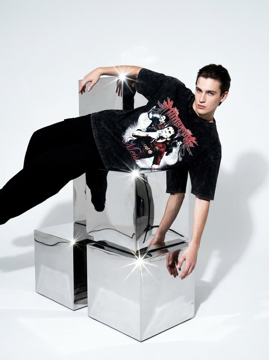minimalist luxury fashion editorial photograph of a stylish subject wearing an oversized black acid-wash t-shirt featuring the attached graphic while laying sideways across stacked chrome cubes inside a seamless white studio, deadpan expression with awkward high-fashion body angles illuminated by aggressive paparazzi flash lighting, reflective metallic surfaces and sharp architectural shadows creating cinematic luxury streetwear campaign atmosphere