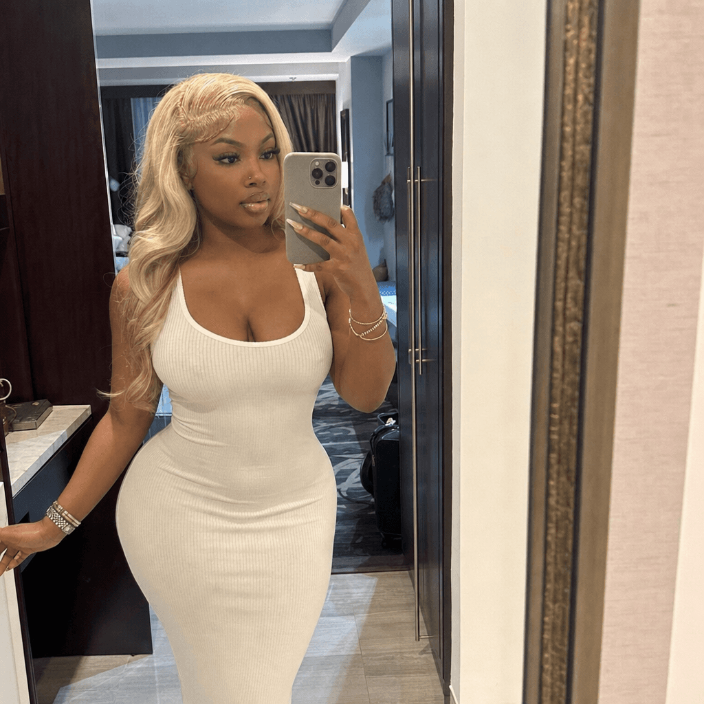 A young ebony woman in her 20s, plump lips, long blonde hair with hair edges, curvy body, thick thighs, plump ass, selfie pov mirror in hotel. Wearing a long bodycon white dress