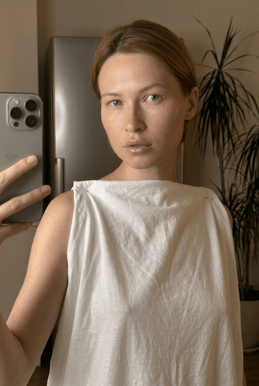 A medium shot captures the person in the uploaded reference image (DO NOT TOUCH FACE). The person's torso is visible from the chest down, with a with a white sheet small mask covering their chest. no tank top. The lighting is soft and warm, with a slightly 24-28mm equivalent lens perspective. The overall tone is intimate and casual
