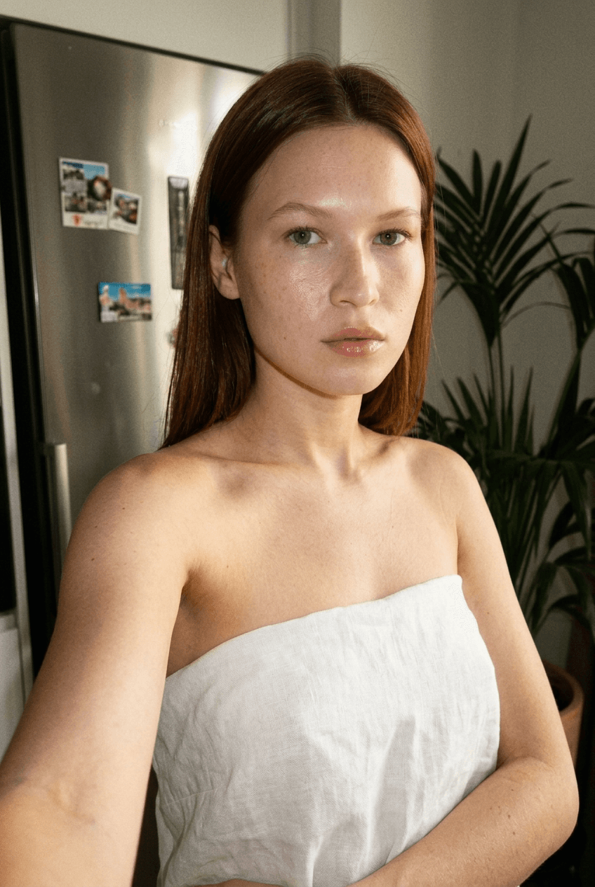 A medium shot captures the person in the uploaded reference image (DO NOT TOUCH FACE). The person's torso is visible from the chest down, with a with a white sheet small mask covering their chest. no tank top. no robe. no towel. The lighting is soft and warm, with a slightly 24-28mm equivalent lens perspective. The overall tone is intimate and casual
