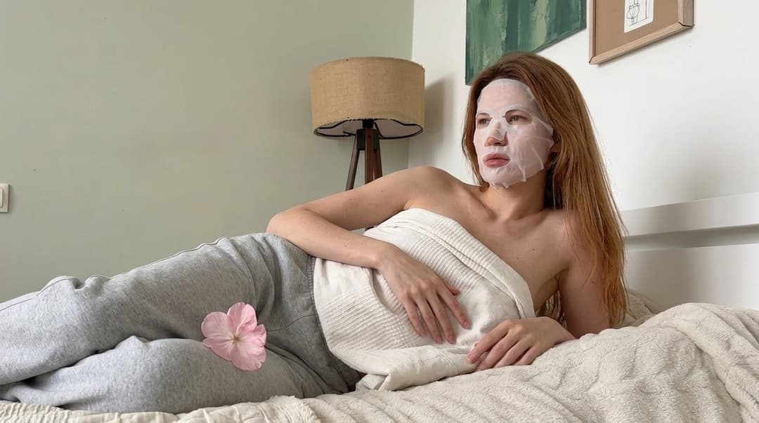 “A medium shot captures the person in the uploaded reference image (DO NOT TOUCH FACE). The person's torso is visible from the chest down, with a with a white sheet small mask covering their chest. The right hand is placed on top of the sheet mask. no tank top. no clothes. The lighting is soft and warm, with a slightly 24-28mm equivalent lens perspective. The overall tone is intimate and casual”